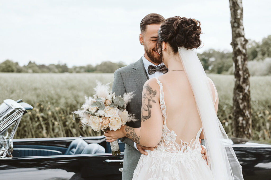 Braut und Bräutigam stehen vor einem Ford Mustang am Feltgenhof in Moers