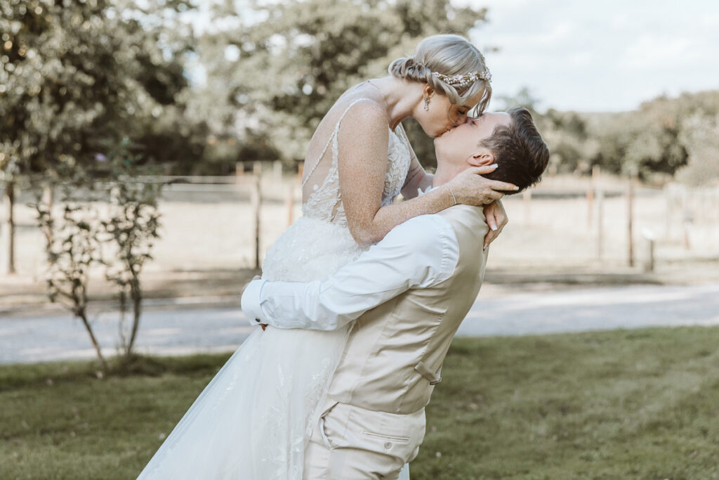 Bräutigam hebt Braut hoch und küsst sie auf dem Landgut Hochwald